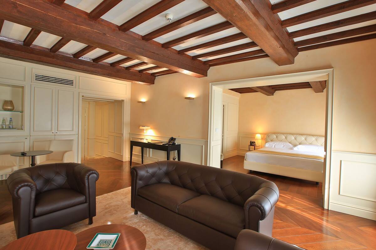 A spacious room with a large bed, a sitting area with two sofas, a small table, and a wooden ceiling with exposed beams.