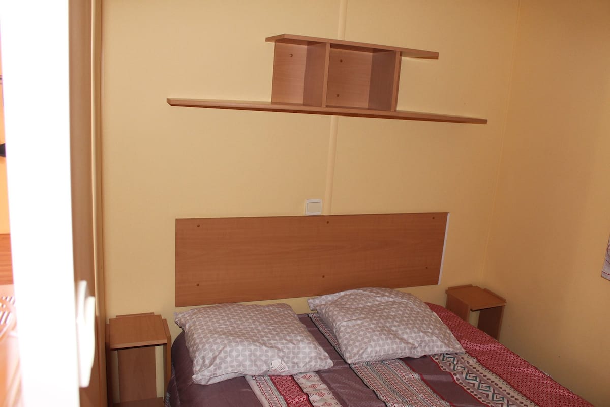 A bedroom with a wooden headboard, two bedside tables, a shelf above the bed, and patterned bedding.