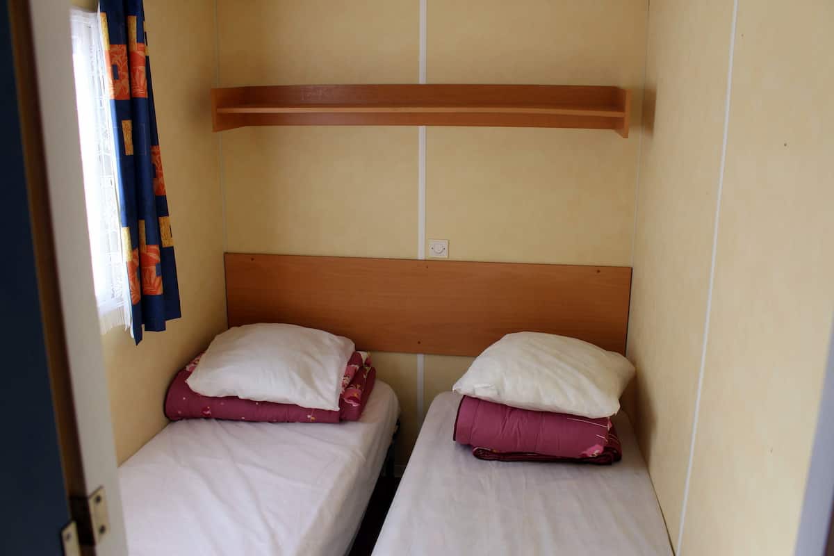 A small, compact room with two single beds, each with a wooden headboard and white bedding.