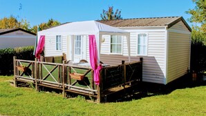 A mobile home with a covered porch, a small deck, and a fenced area. - Camping Le Pontis (Verteillac)