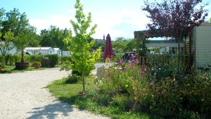 A gravel path leading to a row of mobile homes with a garden area featuring various plants and flowers. - Camping Le Pontis (Verteillac)