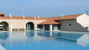 A swimming pool with clear blue water, surrounded by buildings with tiled roofs and white statues. - Camping Le Pontis (Verteillac)