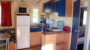 A compact kitchen with a refrigerator, microwave, sink, and stove. - Camping Le Pontis (Verteillac)