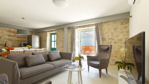 Una sala moderna con un sofá, sillones, una mesita blanca y un televisor de pantalla plana.