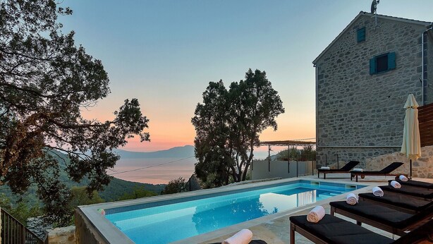 Una piscina con sillones de descanso y un edificio de piedra con vistas al paisaje.