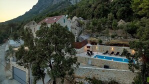 Edificio de piedra con piscina, mobiliario exterior y un paisaje montañoso de fondo.