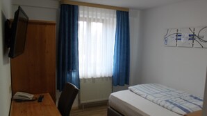 A bedroom with a bed, a desk, a chair, a radiator, and a wall-mounted TV. - Hotel Restaurant Hochdorfer Hirschen (Freiburg im Breisgau)