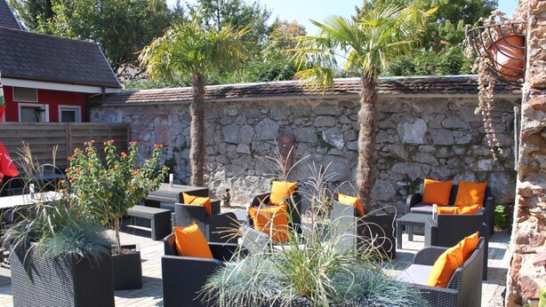 An outdoor seating area with wicker furniture and orange cushions, surrounded by stone walls and potted plants. - Hotel Restaurant Hochdorfer Hirschen (Freiburg im Breisgau)