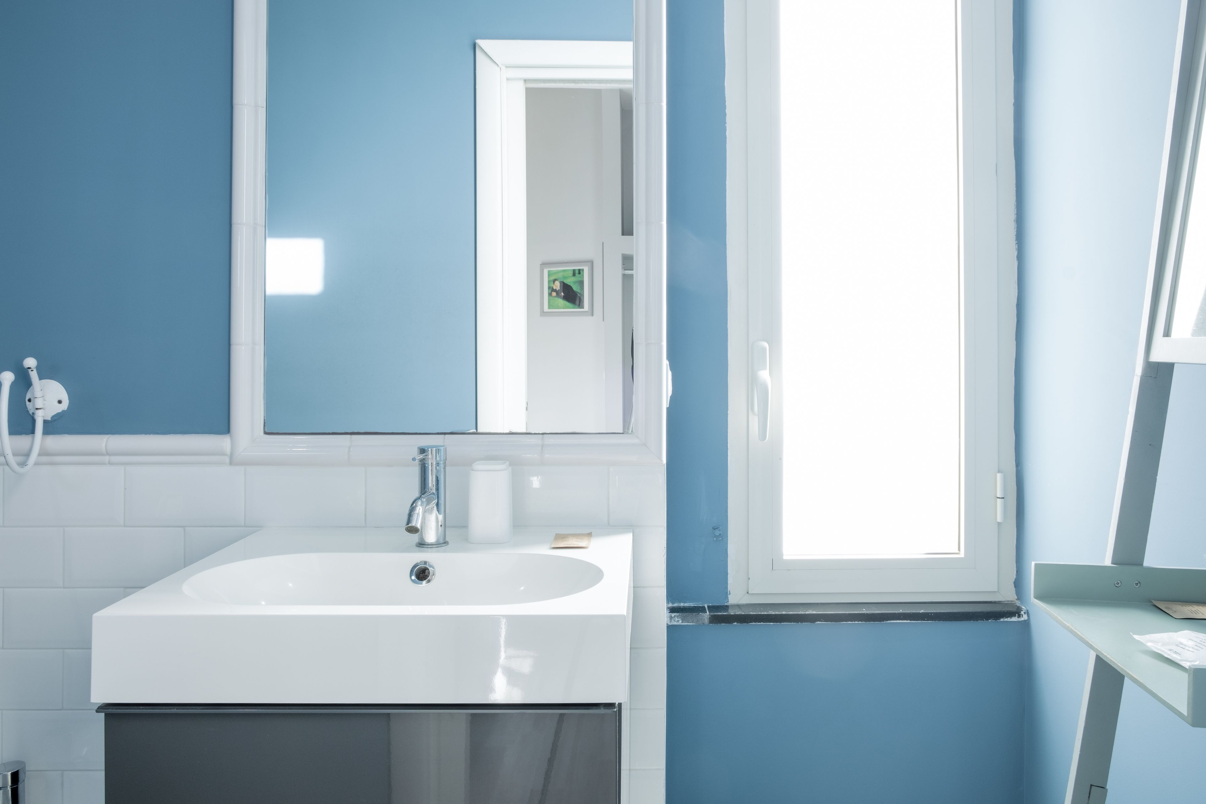 Een badkamer met een wit wastafelmeubel, een spiegel en een raam.
