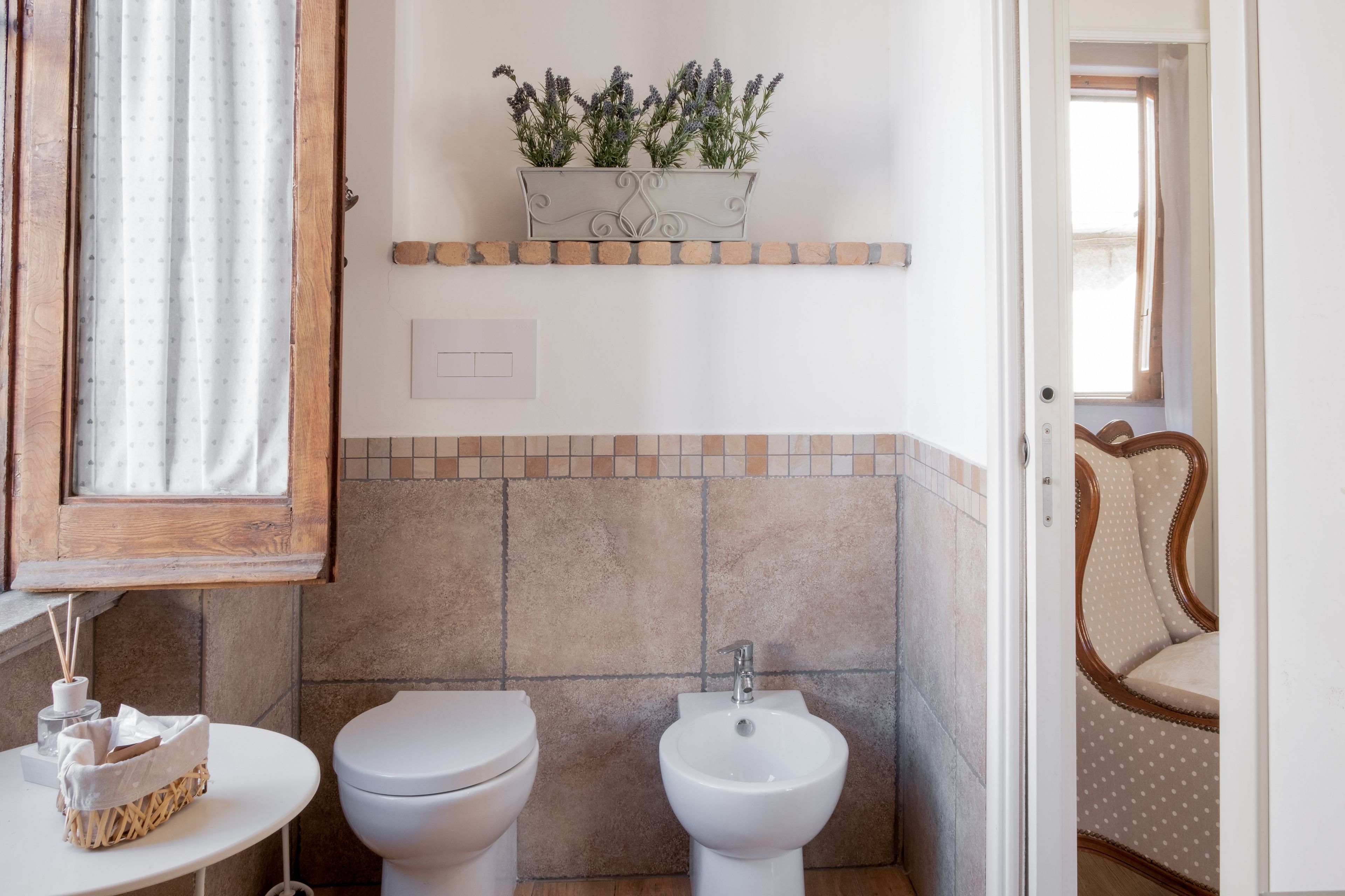 A bathroom with a toilet, bidet, and a small table with a basket.
