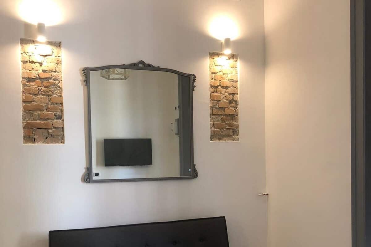 A room with a black sofa, a wooden table, a mirror with a decorative frame, and two wall-mounted lights.