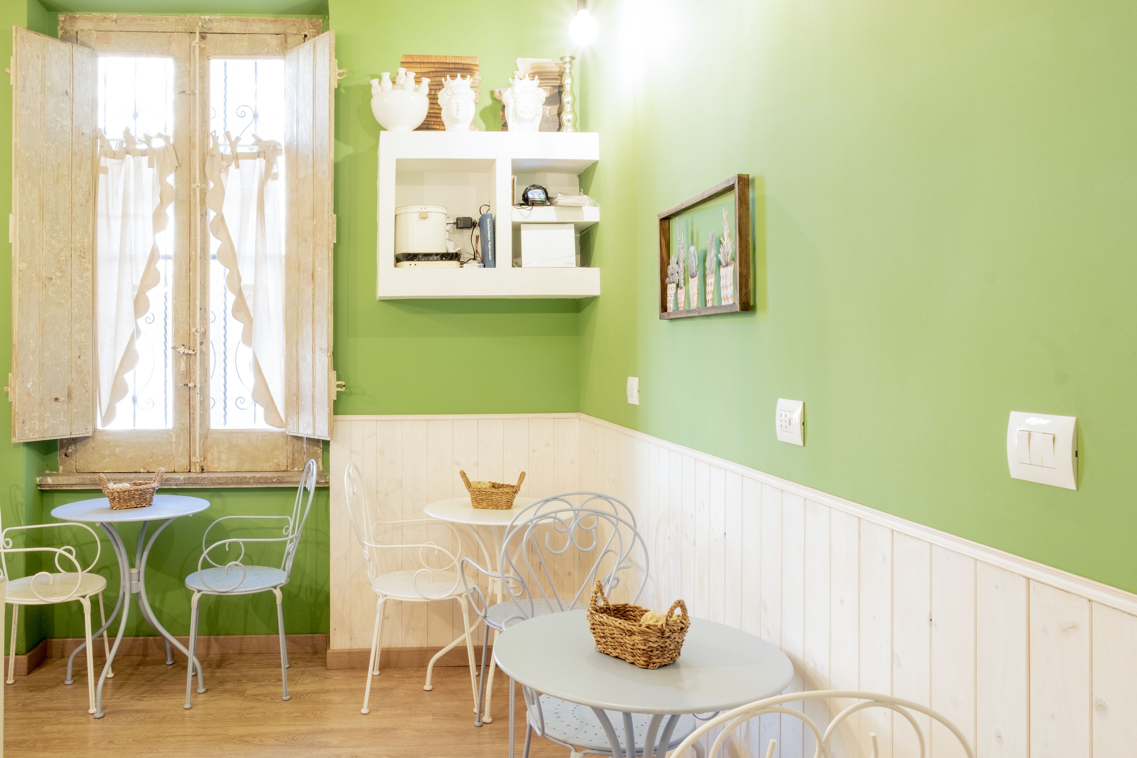A room with a green wall, white furniture, a window with curtains, and a shelf with decorative items.