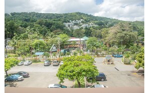 A parking lot with several cars, surrounded by trees and buildings with a mountainous backdrop.