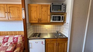A compact kitchenette with wooden cabinets, a microwave, a stove, and a refrigerator. - 2-room apartment with parking in Les Saisies, 4 people, balcony, fully equipped (Les Saisies)