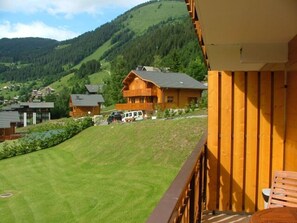 A wooden building with a balcony overlooking a green hillside and a small white car parked in front. - Cozy apartment in Châtel - 4 ppl, balcony, parking (Châtel)