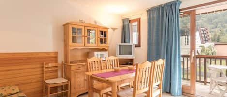 Una habitación acogedora con una mesa de madera, sillas, un armario, un televisor y un balcón con vistas al paisaje.