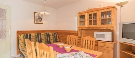 Una sala de estar acogedora con un sofá de madera, una mesa de comedor con sillas, un armario con puertas de cristal, un microondas y una televisión.