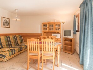 Ett vardagsrum med en soffa, trästolar, ett matbord, en tv och ett köksområde med skåp och en mikrovågsugn.