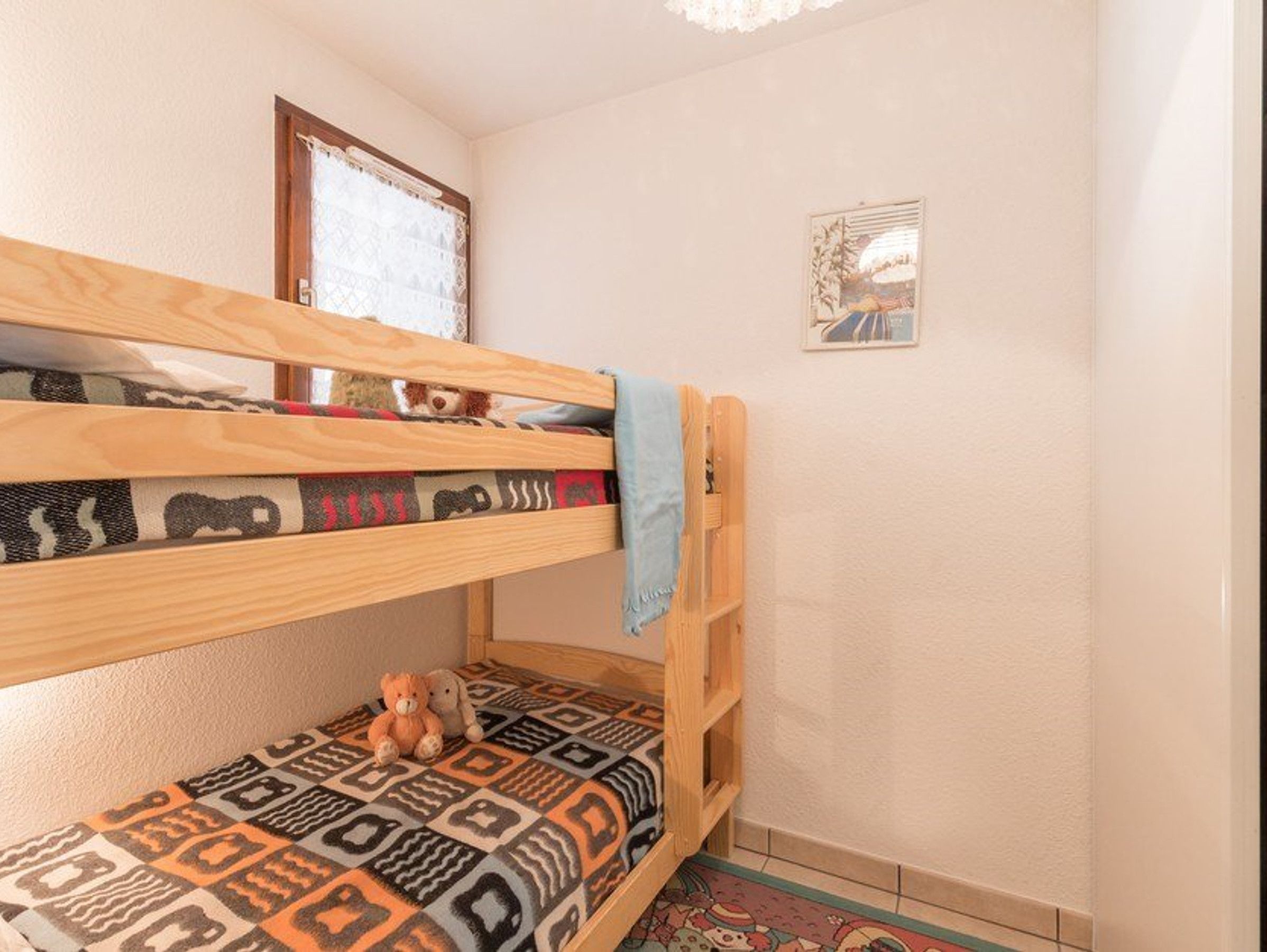 Un lit superposé avec une couverture à motifs et un ours en peluche sur le lit du bas.