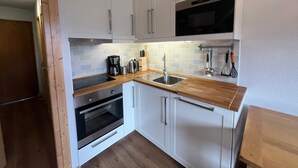 A compact kitchen with white cabinets, a wooden countertop, a built-in oven, a microwave, and a hanging utensil rack. - 2-room apartment for 4 people with balcony in Châtel (Châtel)