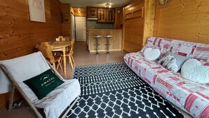 A cozy cabin interior with a dining area, kitchenette, and a sofa with patterned bedding. - Cozy studio with south-facing balcony and parking (Châtel)