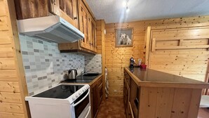 A compact kitchen with wooden cabinets, a tiled backsplash, a stove, and a sink. - Cozy studio with south-facing balcony and parking (Châtel)
