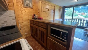 A kitchen with wooden cabinets, a built-in dishwasher, and a large window offering a view of the outdoors. - Cozy studio with south-facing balcony and parking (Châtel)