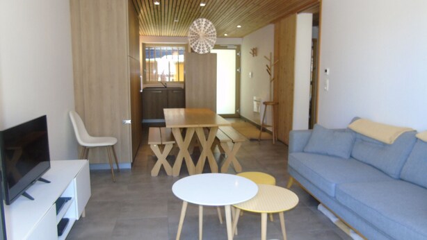 A modern living room with a TV, seating, a dining table, and a kitchen area in the background. - Comfortable apartment in Châtel with balcony for 4 pers. (Châtel)