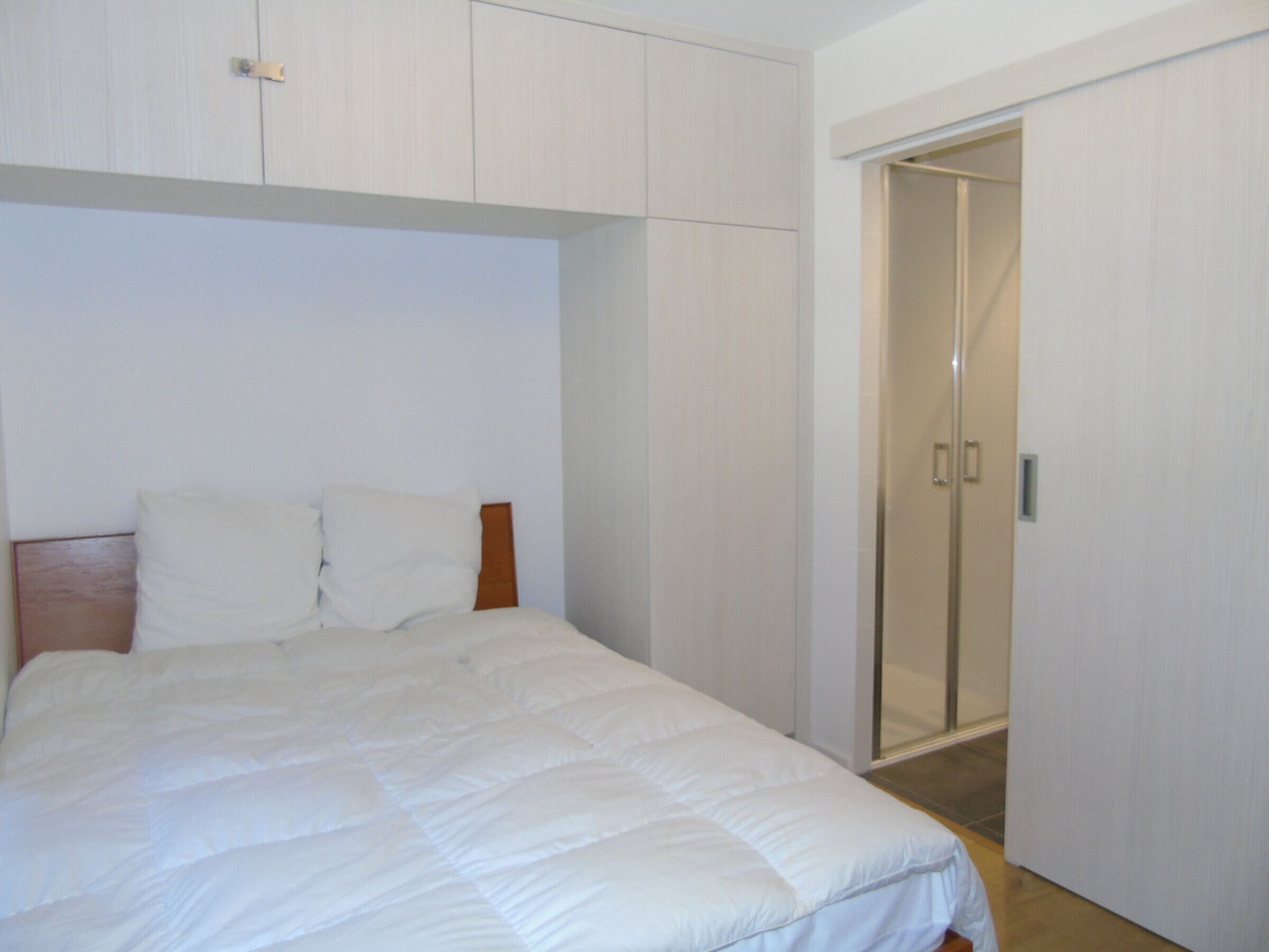 Une chambre à coucher avec un lit, une tête de lit en bois, un mur blanc et un placard à portes coulissantes.