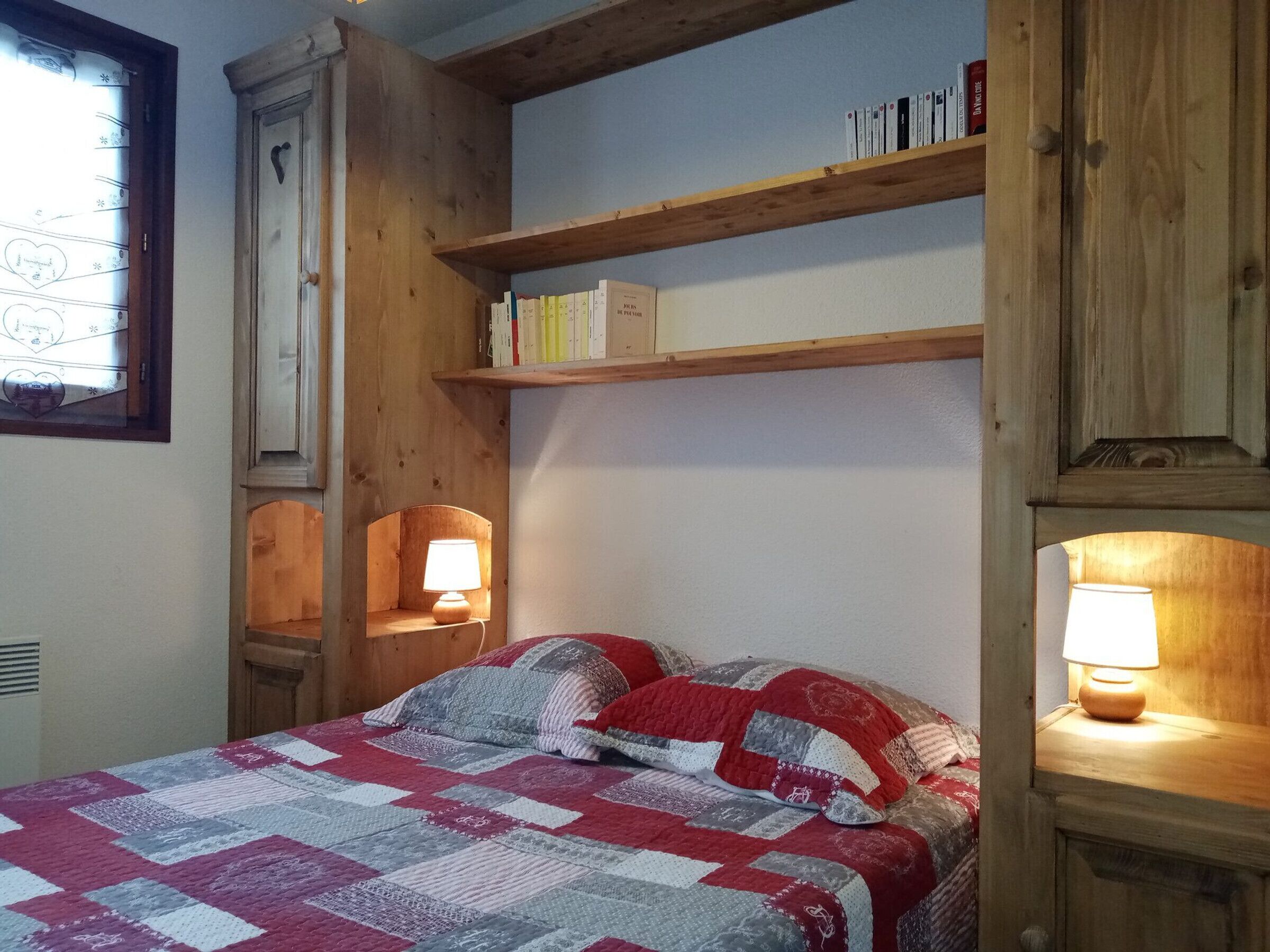 Une chambre à coucher avec un lit, des étagères en bois, une fenêtre et une lampe.