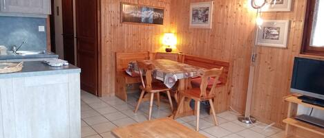 A cozy room with a wooden dining table, chairs, a small kitchen area with a sink, and a television.