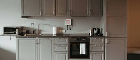 A modern kitchen with grey cabinets, a microwave, a sink, a kettle, and an oven.