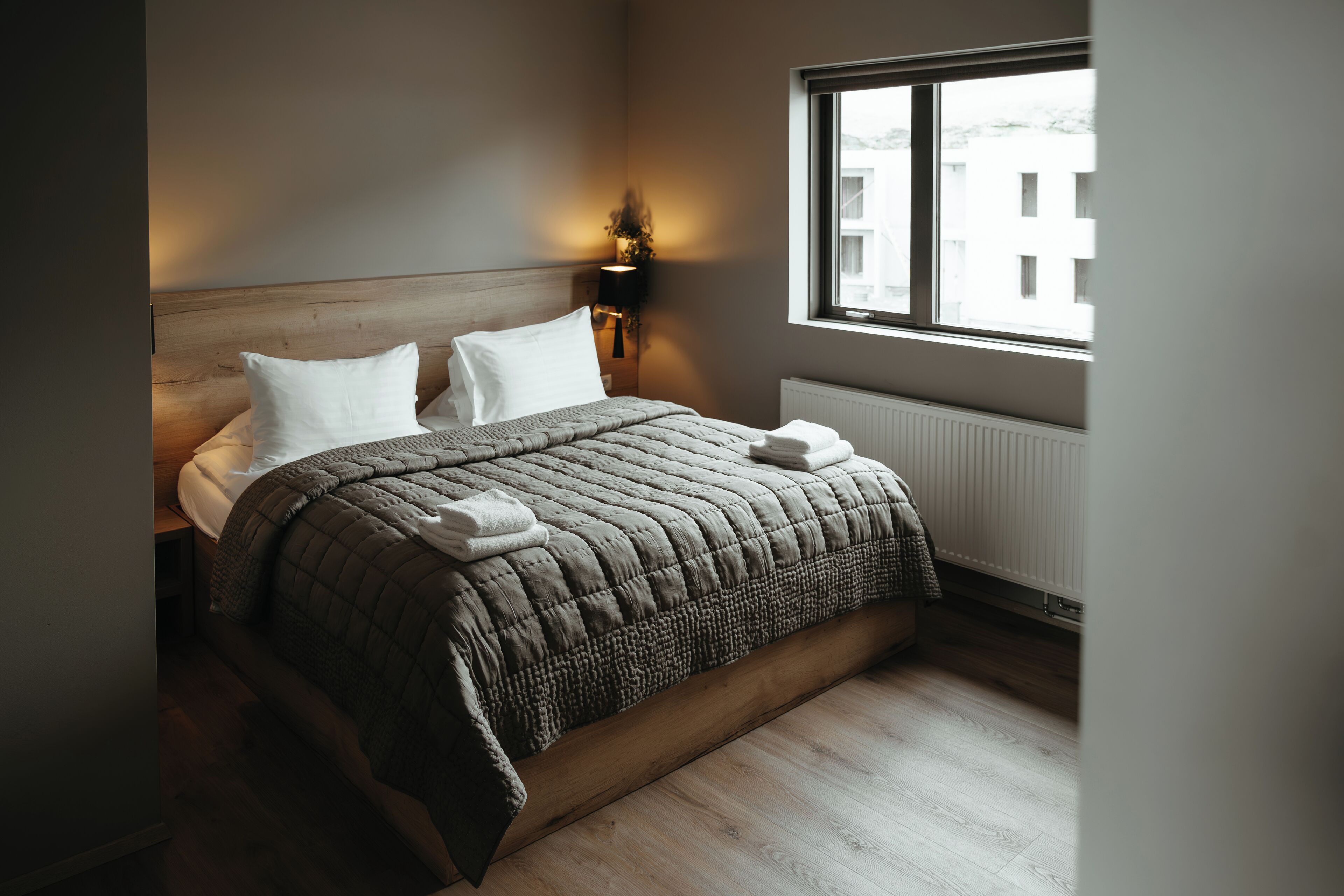 Una cama bien hecha con un edredón acolchado, dos almohadas y una lámpara de noche.