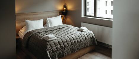 Una cama bien hecha con un edredón acolchado, dos almohadas y una lámpara de noche.