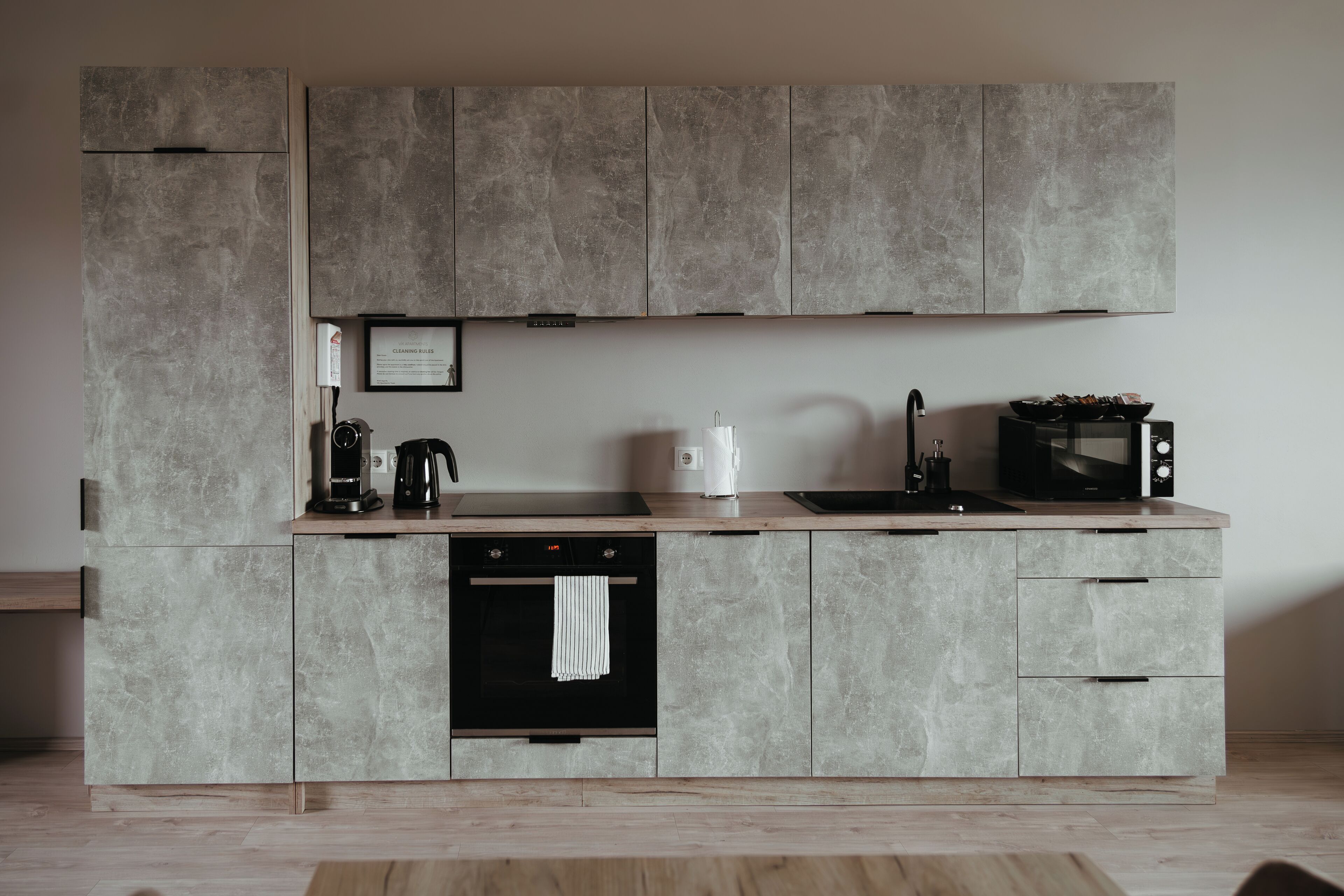 Uma cozinha moderna com armários cinza, forno embutido, cafeteira, torradeira e micro-ondas.
