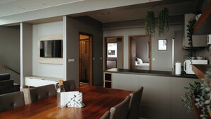 A modern dining area with a wooden table and chairs, a kitchen in the background, and hanging plants. - Vík Apartments (Vik I Myrdal)