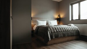A modern bedroom with a large bed, a nightstand, a lamp, and a window. - Vík Apartments (Vik I Myrdal)