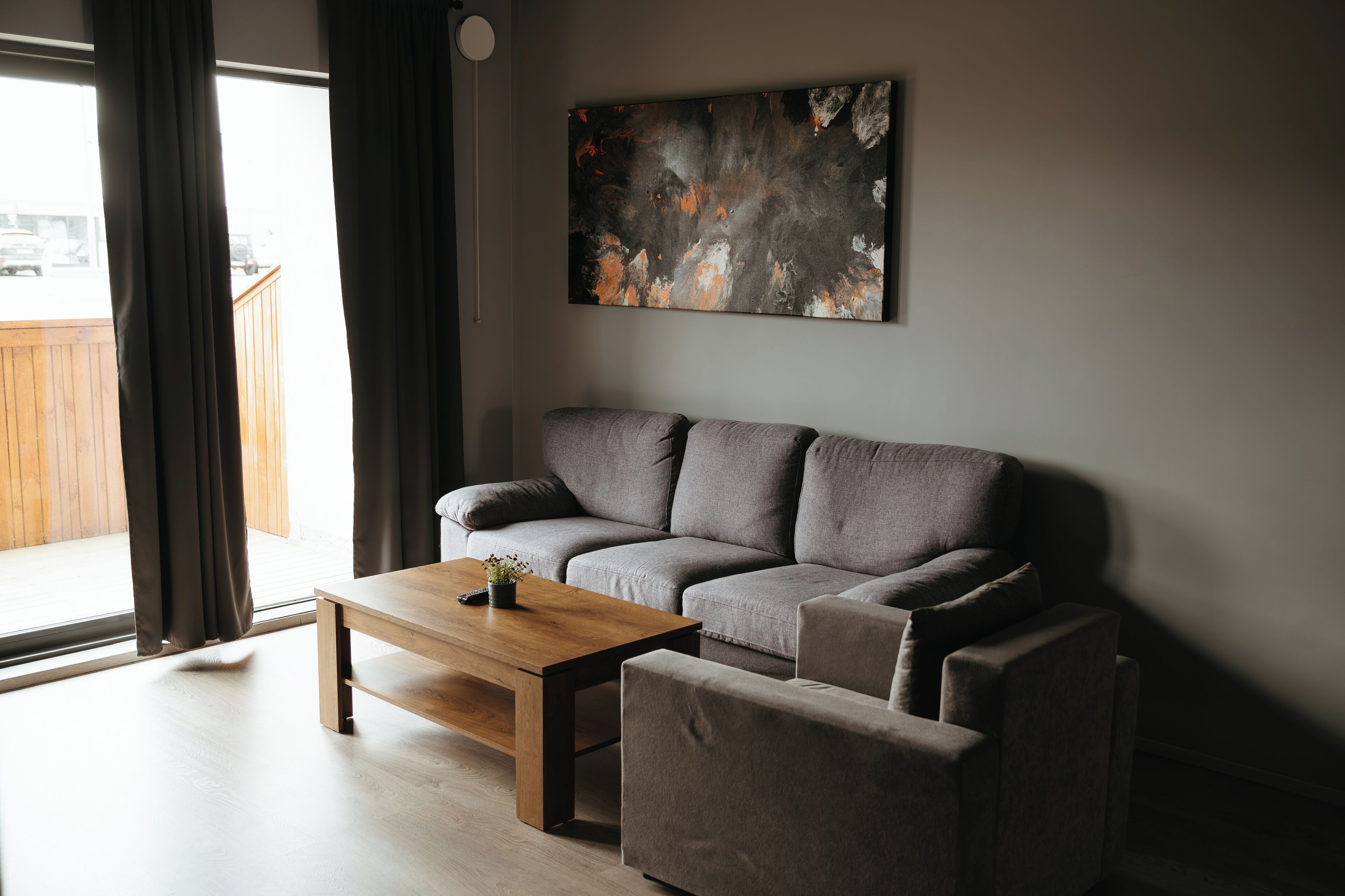 Un salon moderne avec un canapé gris, une table basse en bois et un tableau accroché au mur.