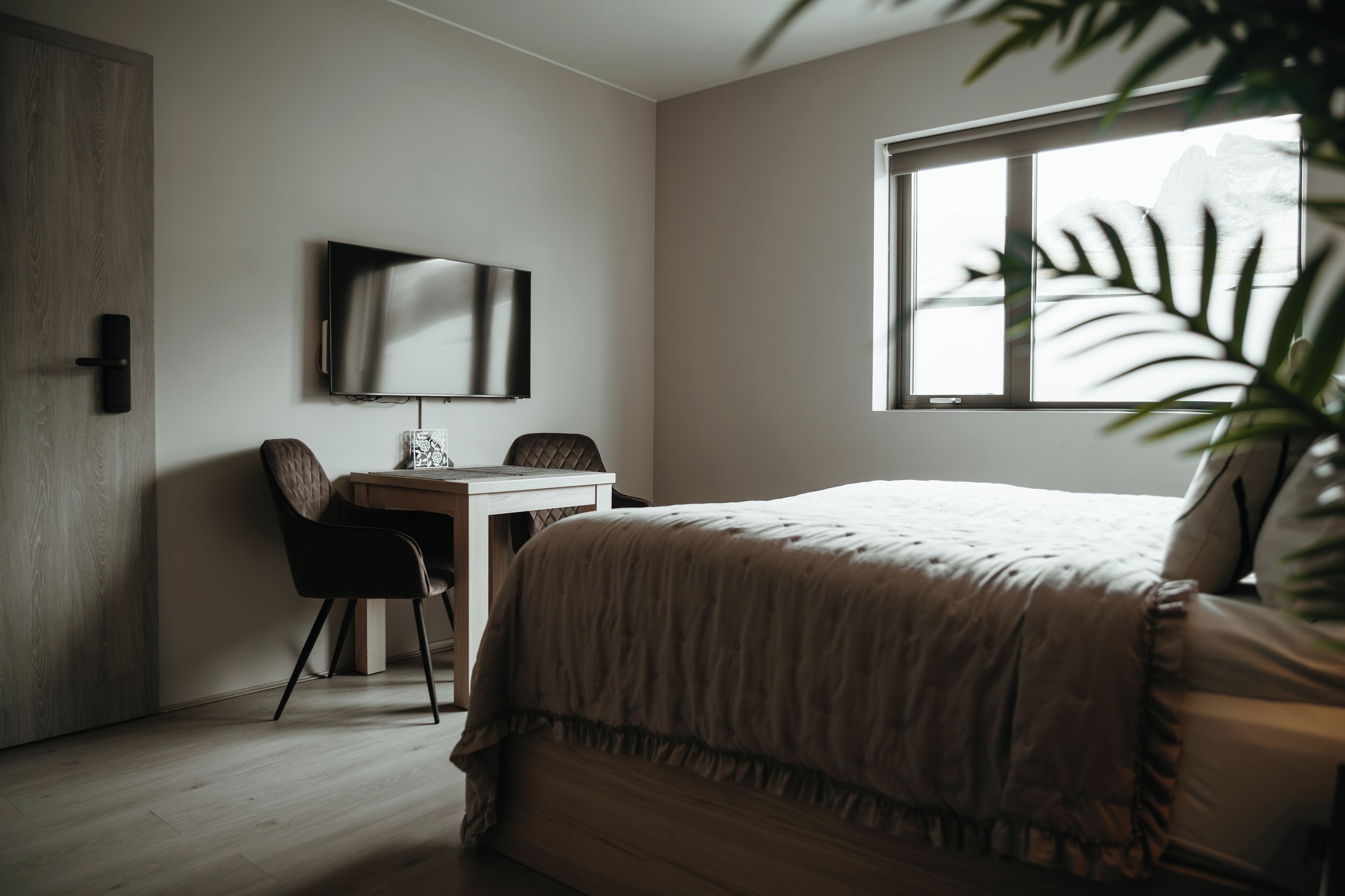 A bedroom with a bed, a desk, a chair, a TV, and a window with a view.
