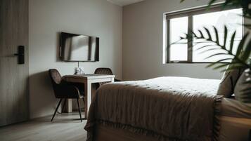 A bedroom with a bed, a desk, a chair, a TV, and a window with a view.