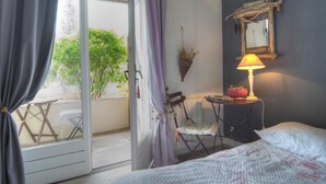 A bedroom with a bed, a chair, a table, a lamp, and a view of greenery outside. - Chambres d'hotes Maison Prairie Bonheur (Magny-les-Hameaux)