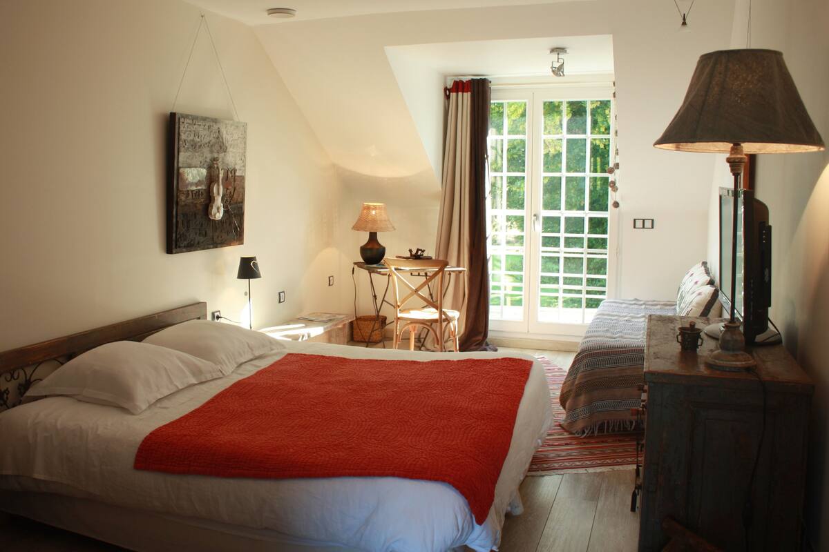 Une chambre à coucher avec un lit, un bureau, une chaise, une lampe et une fenêtre avec des rideaux.