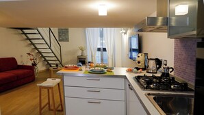 A compact kitchen with a gas stove, a sink, and a small dining area with a table and chairs. A staircase is visible in the background leading to another level. - CATANIA HISTORICAL CENTER APARTMENT - LA PETITE SUITE ON 2 LEVELS. (catania)