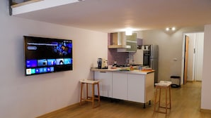 A modern kitchen with a flat-screen TV mounted on the wall, wooden stools, a stainless steel refrigerator, and a compact island. - CATANIA HISTORICAL CENTER APARTMENT - LA PETITE SUITE ON 2 LEVELS. (catania)