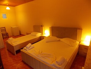 A hotel room with two single beds, each with a pillow and a rolled towel. There is a chair and a small table with a lamp. - Hotel Riviera (Himarë)