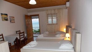 Habitació amb dos llits, una taula de fusta, cadires, una finestra amb cortines i vista al mar.