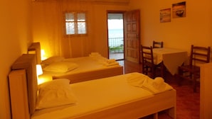 Habitació amb dos llits, una taula, cadires, una finestra amb cortines i una porta que dóna a l'exterior.