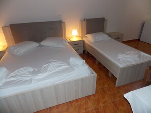 A hotel room with two single beds, a large bed, and a nightstand with a lamp. - Hotel Riviera (Himarë)