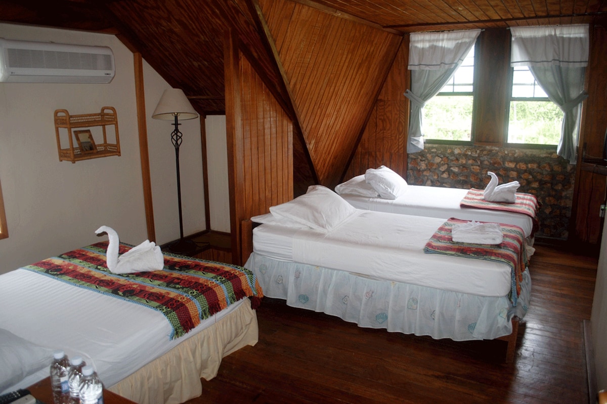 A room with two beds, a wooden ceiling, a stone wall, and a window with curtains.