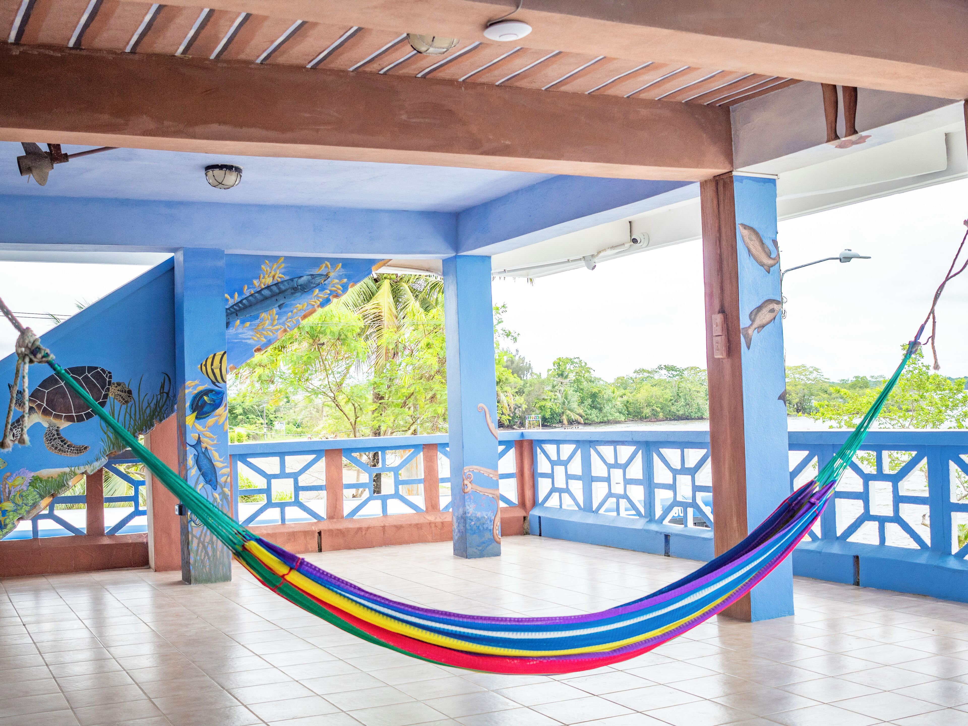 Una hamaca en un espacio exterior techado con paredes azules y un mural de criaturas marinas.